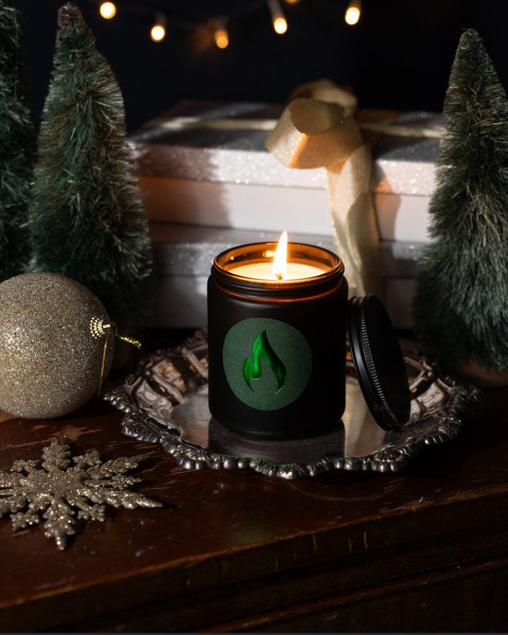 Candle with a green logo on a decorative tray with Christmas decor